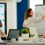 Mujer señalando una pizarra con gráficos de ventas
